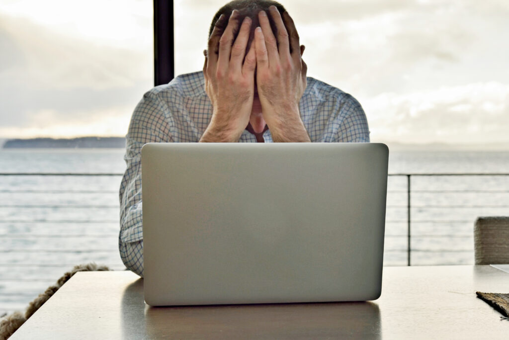 computer-burnout-man-with-hands-covering-face-while-working-with-a-laptop-computer-frustration-stress