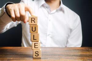 A man holds a tower of blocks with the word Rules from falling. Setting clear rule and restrictions. Leadership and discipline. Authoritarianism, tight control framework. Norms and laws in society