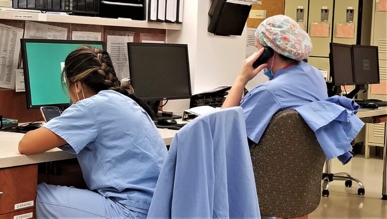a-doctor-on-the-phone-after-performing-surgery-on-a-patient-as-the-nurse-works-at-her-computer-on-the_t20